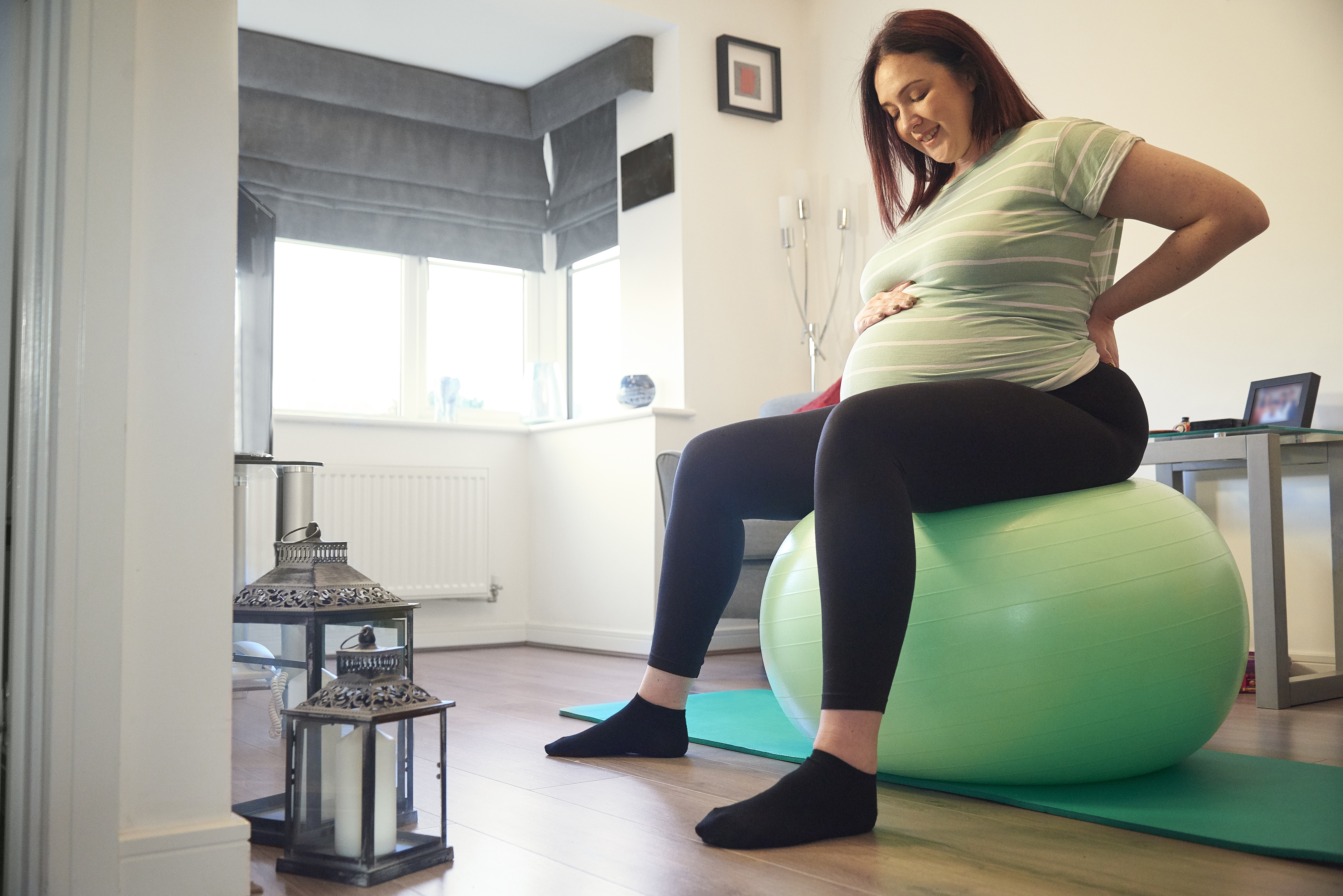 Pregnant Woman sitting and stretching on medicine ball